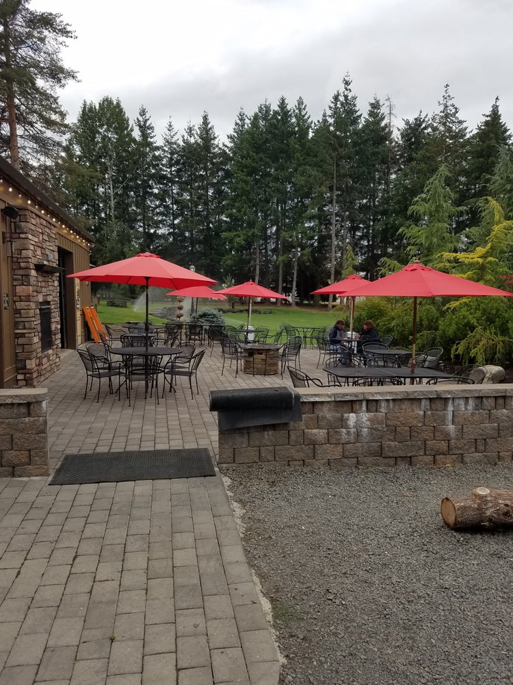 The outdoor patio, with grass and trees in the background. The patio tables have a red umbrellas over them.