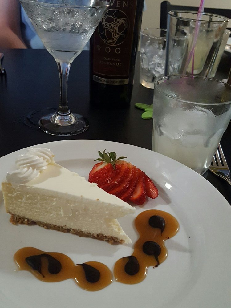 A piece of white cheesecake with a sliced strawberry and dollops of what look like chocolate and caramel on the plate.
