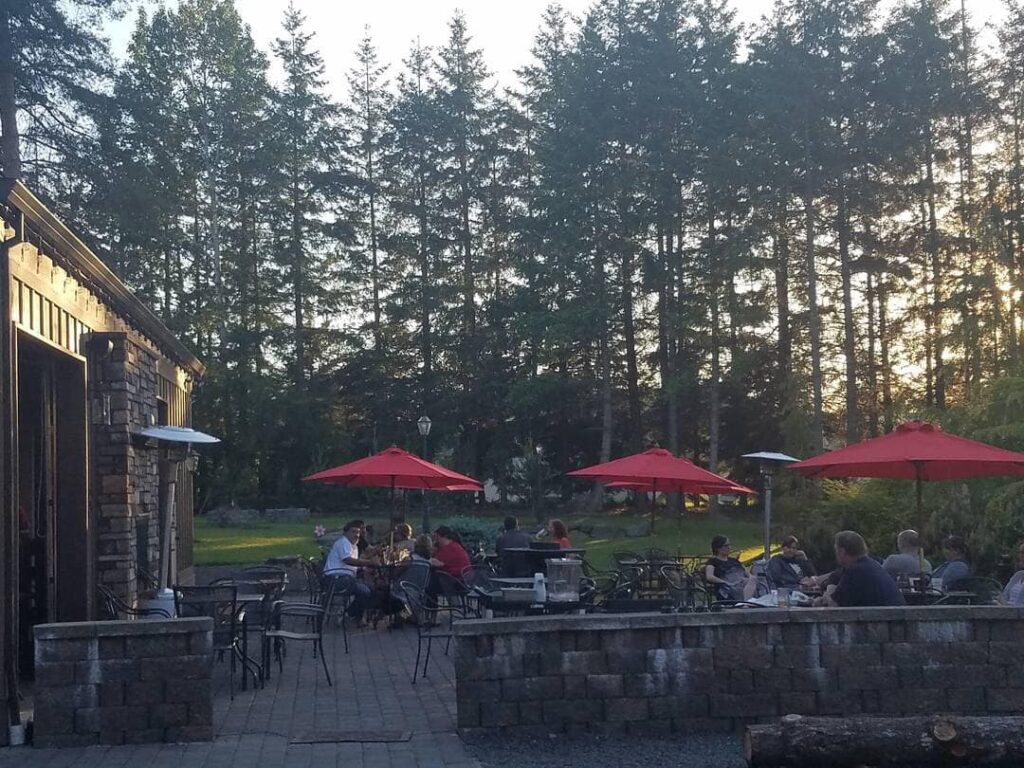 The outdoor patio, with grass and trees in the background. The patio tables have a red umbrellas over them.