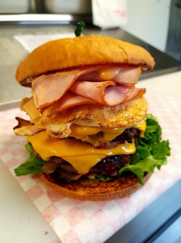 A huge burger with cheese, lettuce, and what looks like ham and egg. Looks delicious.