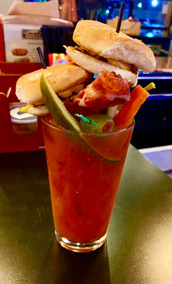 A red alcoholic drink with two burger sliders and vegetables on top.