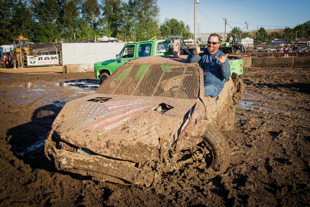 A man poses in a very muddy car from the demolition derby