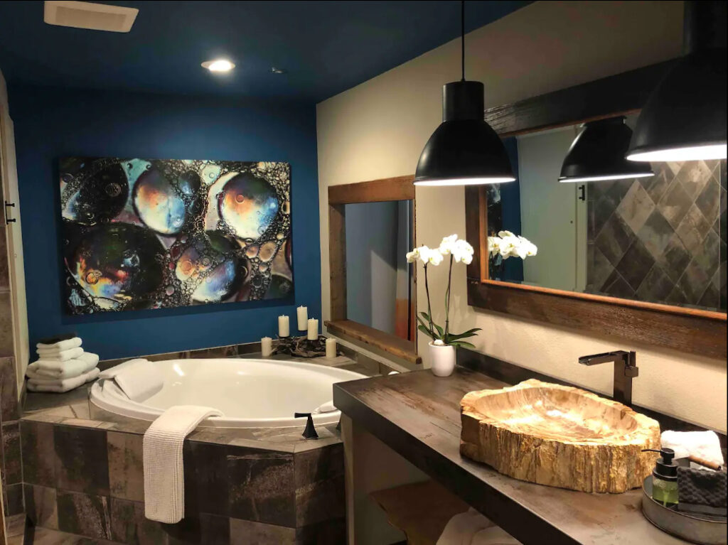 A huge soaking tub sits in the corner of a bathroom painted in cream and dark blue. There's a petrified wood sink next to the tub.