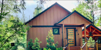 The exterior of the cabin. It's painted light brown and has a modern front door with horizontal windows and steps leading up to it.