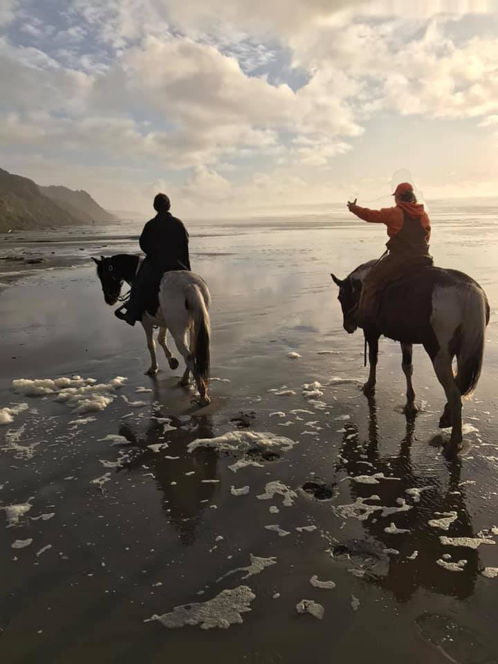 Two people ride white horses along the beach in Bandon Oregon.