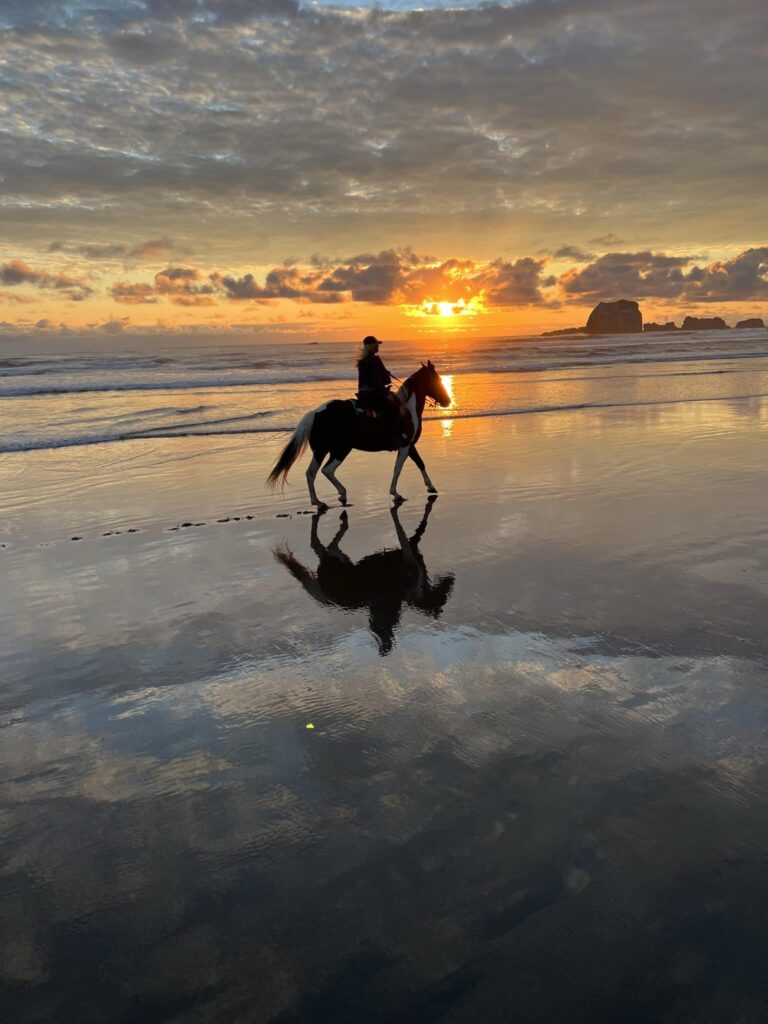 A lone rider rides on wet sand on the beach in Bandon at sunset. It's a peaceful looking scene.