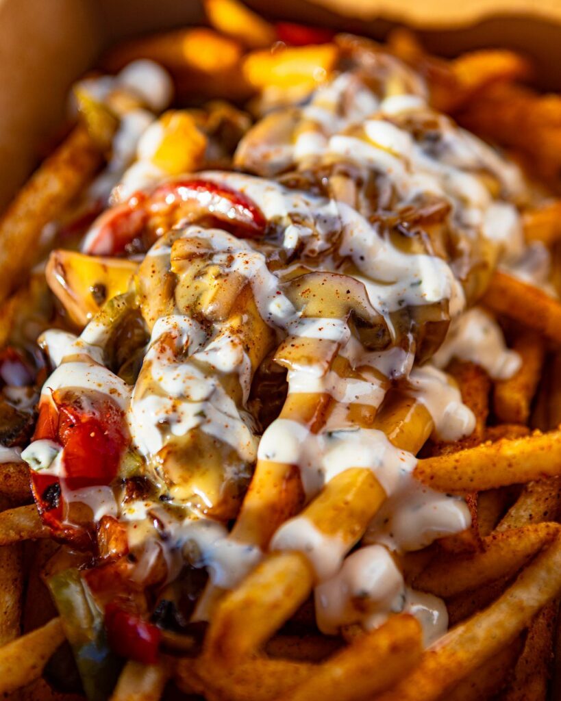 A basket of French fries drizzled in sauce and sprinkled with seasoning, heaped with toppings.