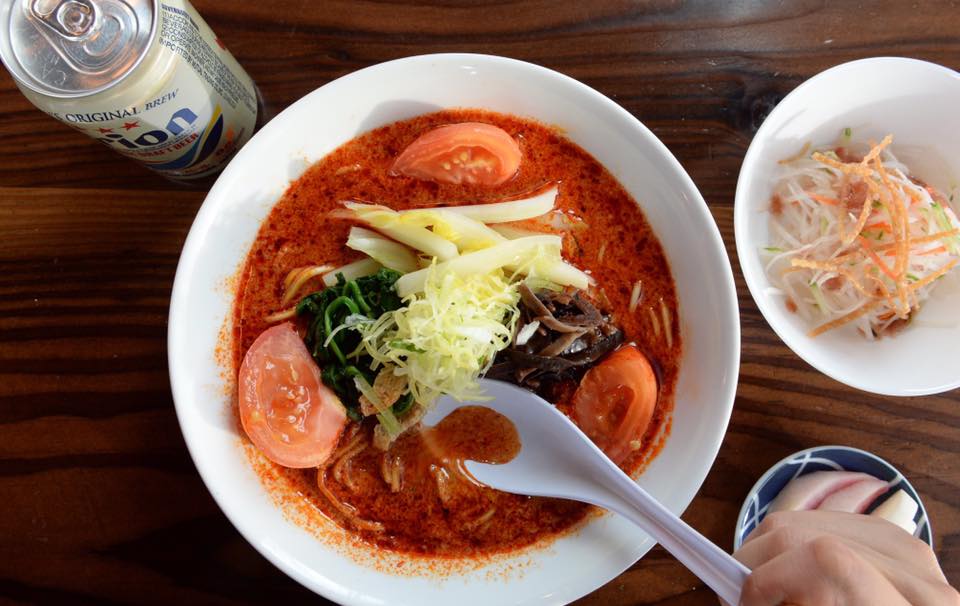 A creamy and delicious looking bowl of bright red ramen with green and white vegetables on top at Kinboshi Ramen in Portland, Oregon.