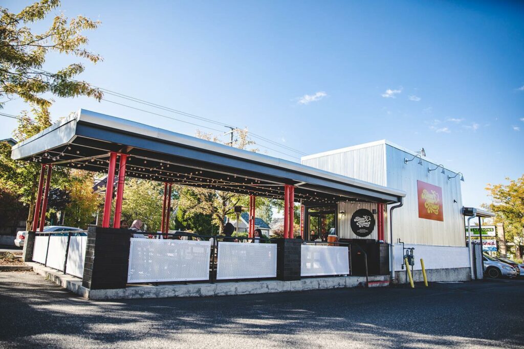 The exterior of Bless Your Heart Burger in Portland. There's a walkup window and a covered outdoor seating area with red pillars.