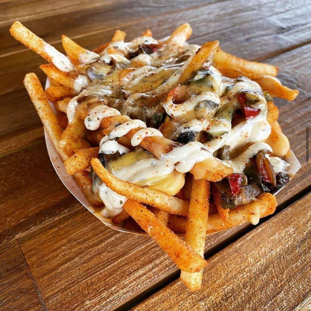 A basket of French fries drizzled in sauce and heaped with toppings.