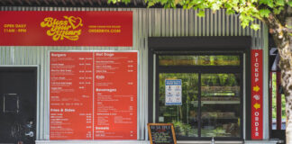 The walkup order window at Bless Your Heart Burgers. The building has metal siding and bright red signs with yellow lettering.