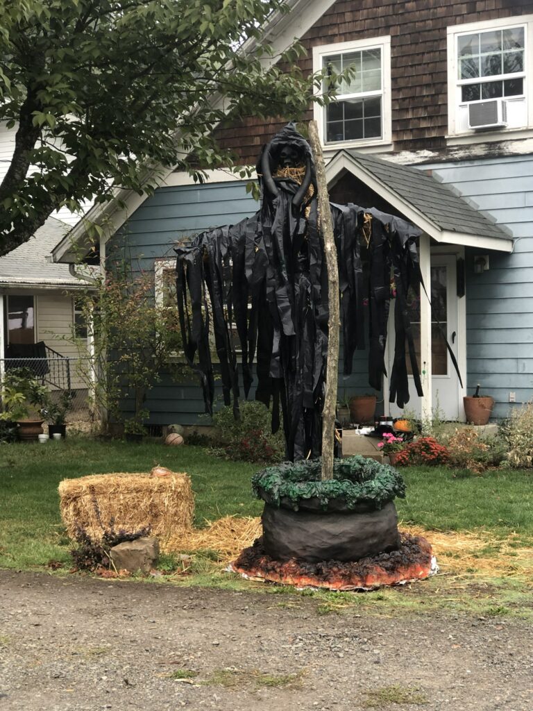 A super scary scarecrow with black rags hanging off of it in a front yard. It's tall.