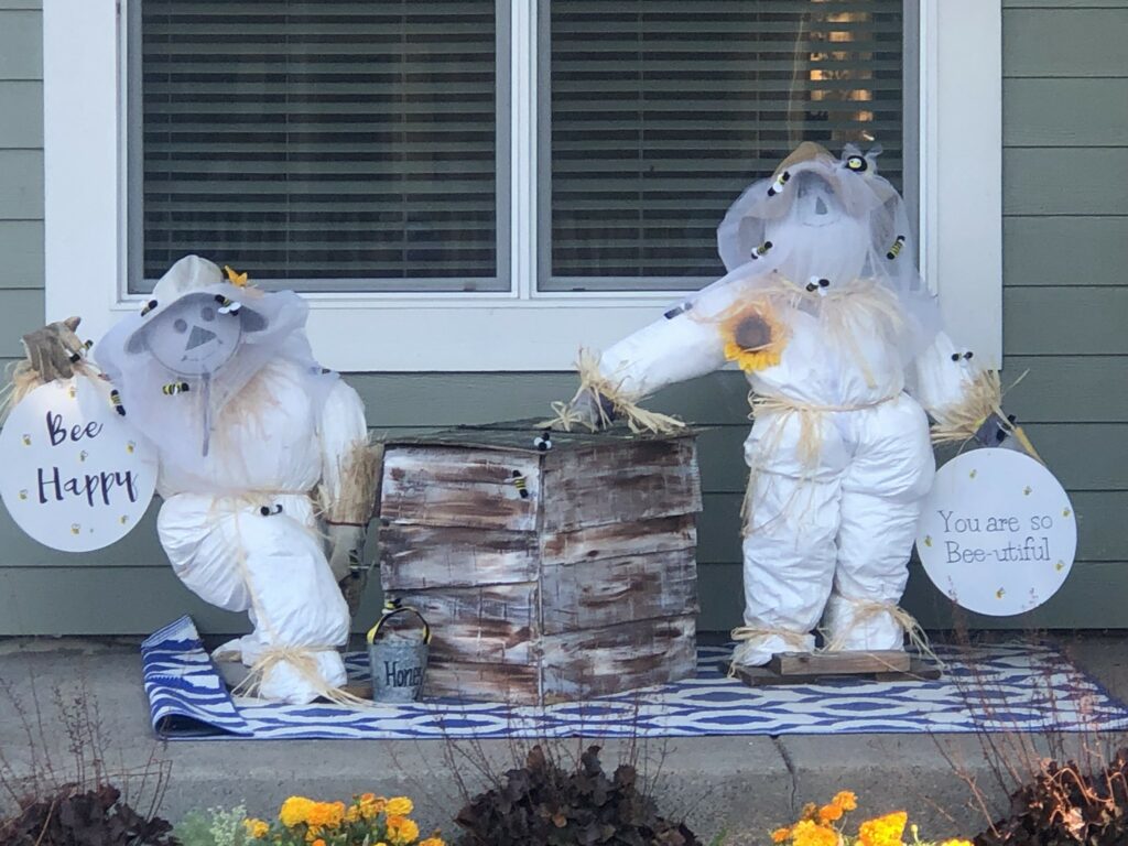 Two honey bee keeper scarecrows on a front porch.