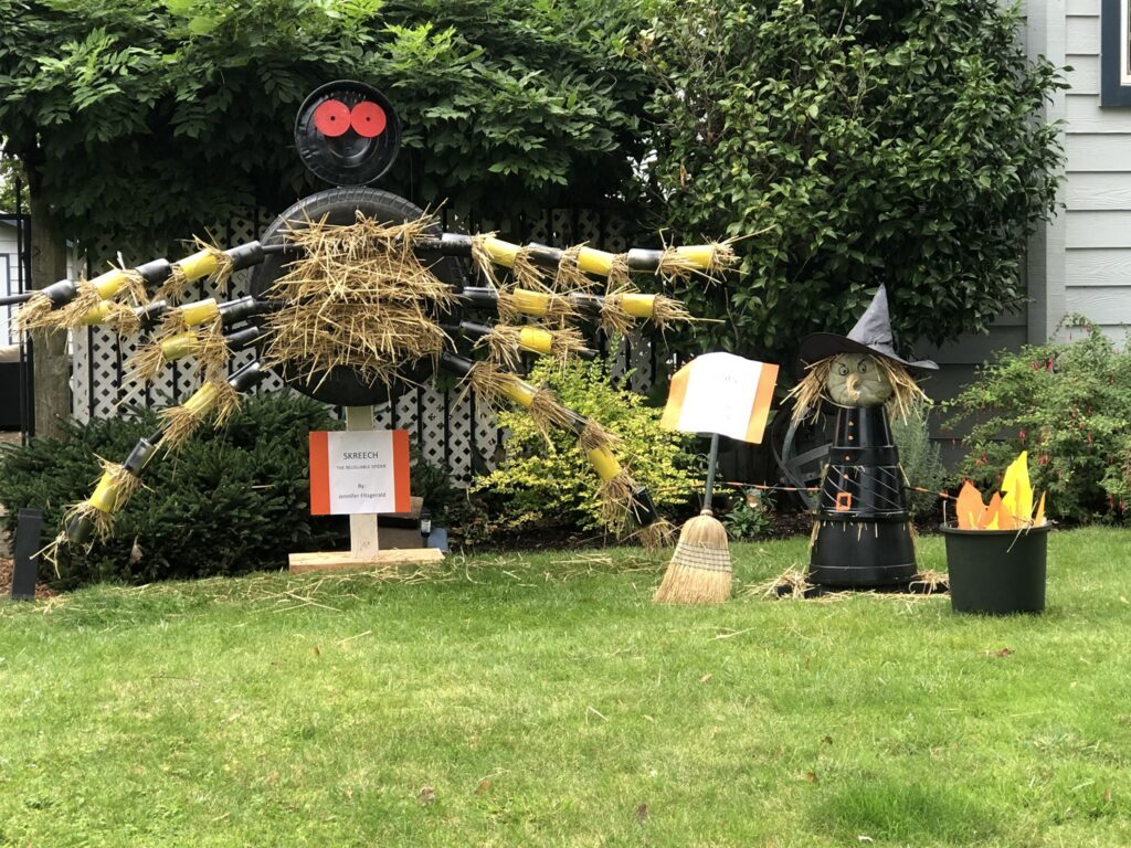 A spider scarecrow next to a witch scarecrow in a yard.