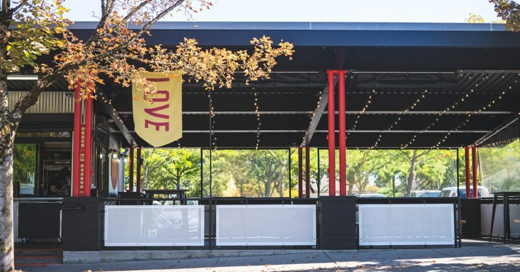 The exterior of Bless Your Heart Burger in Portland, Oregon. There's a covered eating area with picnic tables.