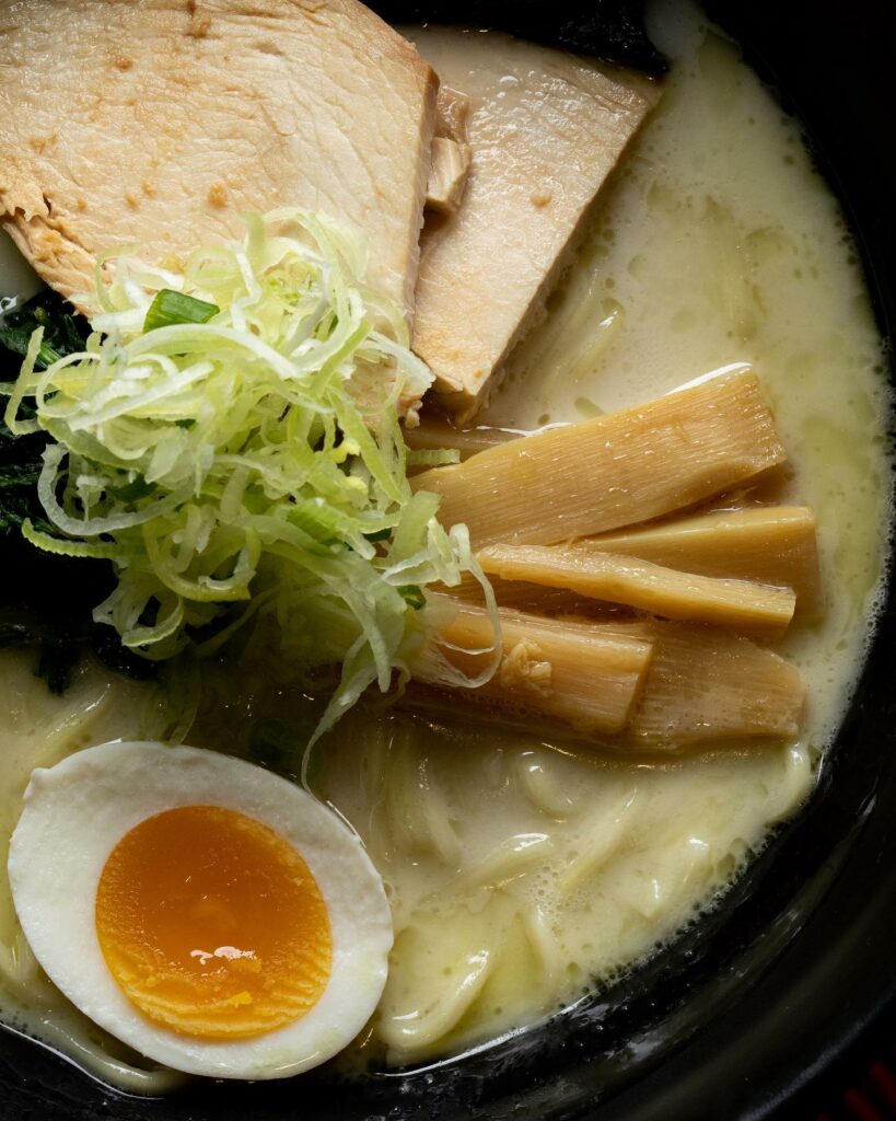 A creamy bowl of ramen with a boiled egg, and green vegetables on top.
