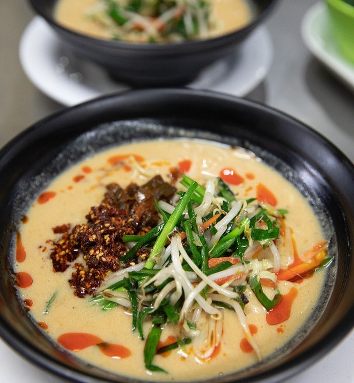 A bowl of delicious creamy looking ramen ramen with colorful green, yellow and red toppings.