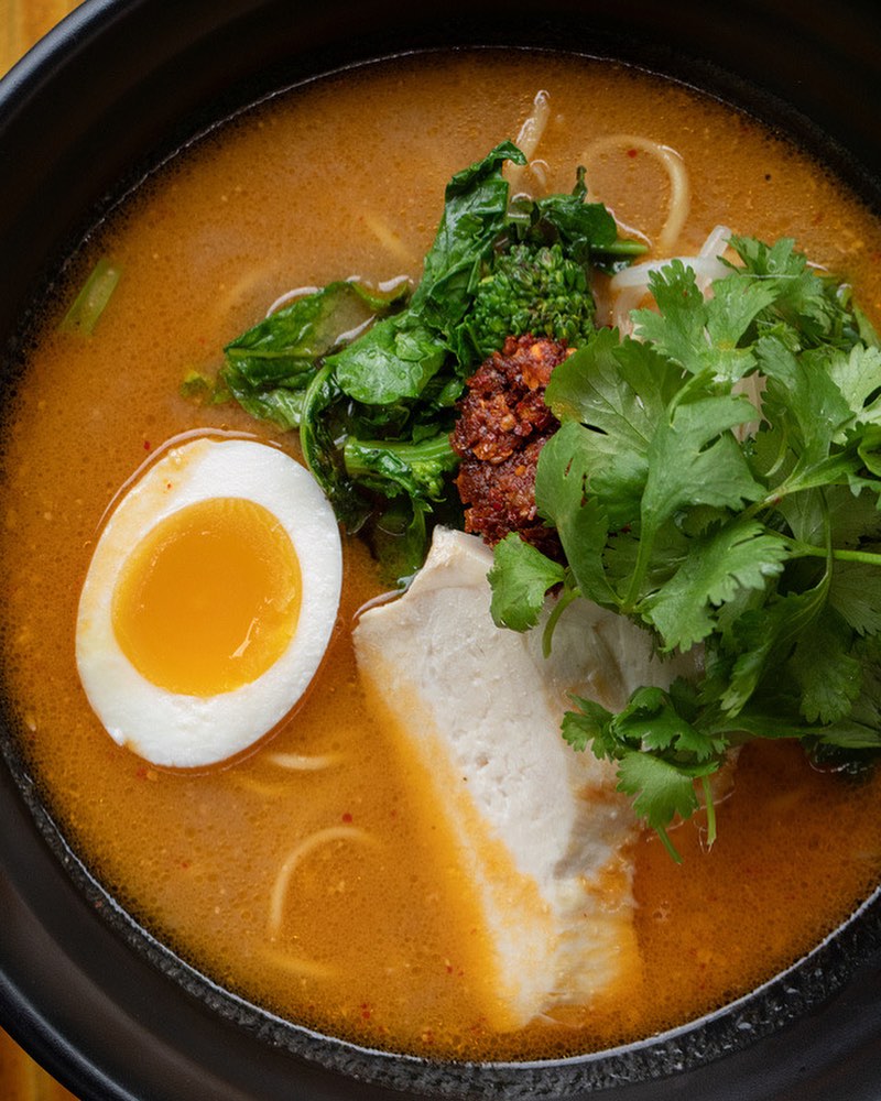 A bowl of delicious ramen with colorful vegetables, egg, and yellow soup.