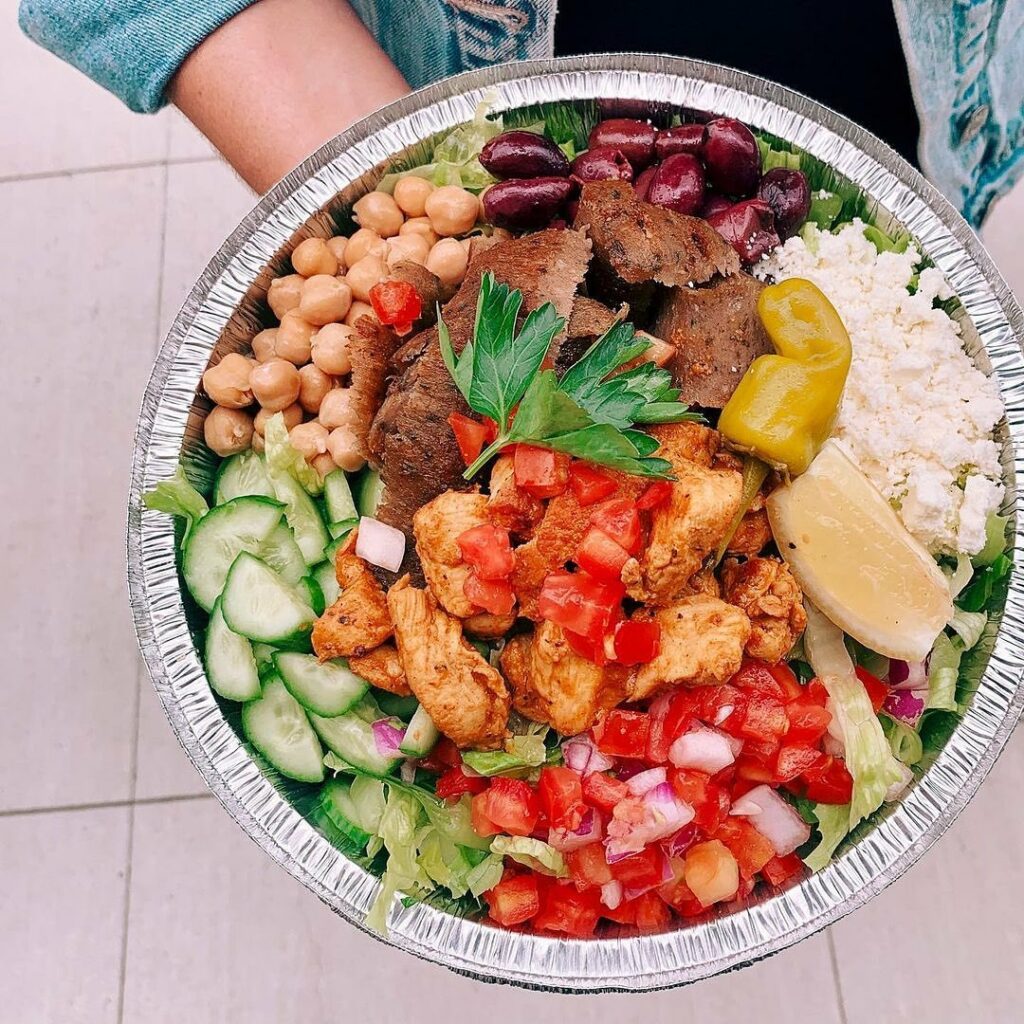 A colorful bowl full of meat, cucumbers, beans, tomatoes, and other food.