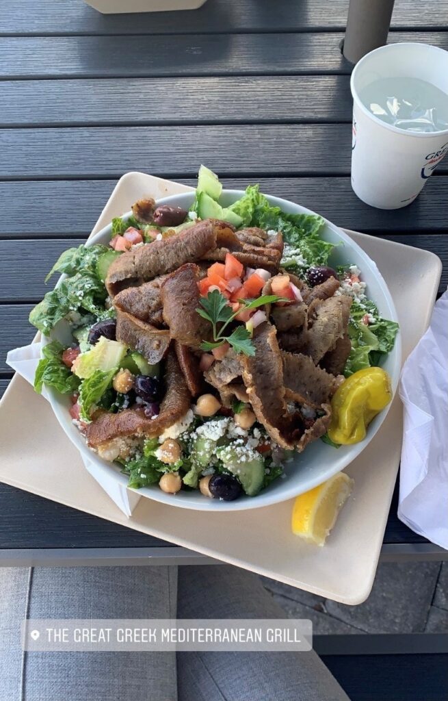 A plate of Greek food with meat, cheese crumble and greens.