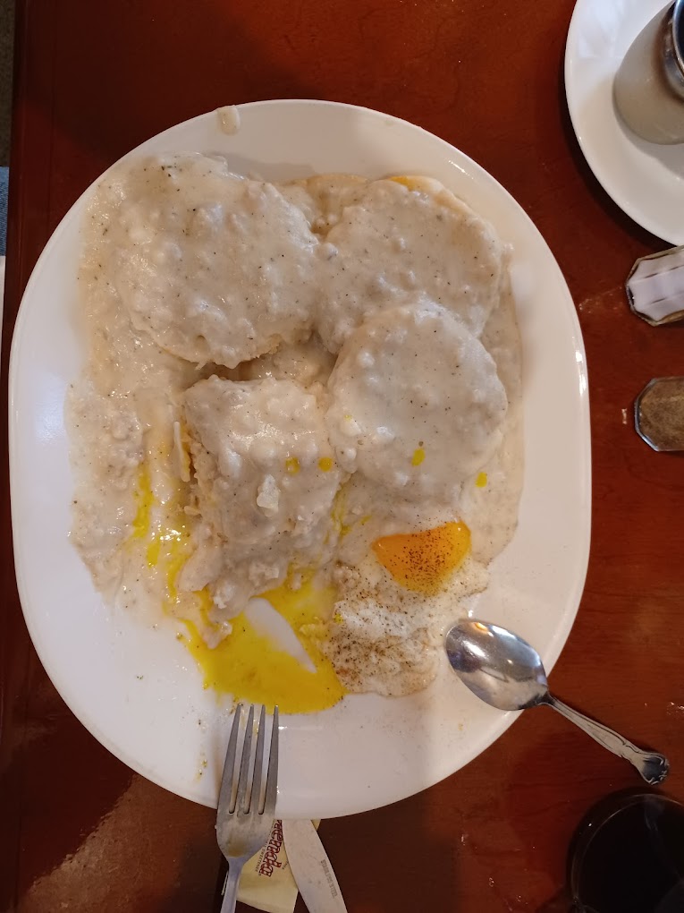 Biscuits and gravy with eggs on a white plate.