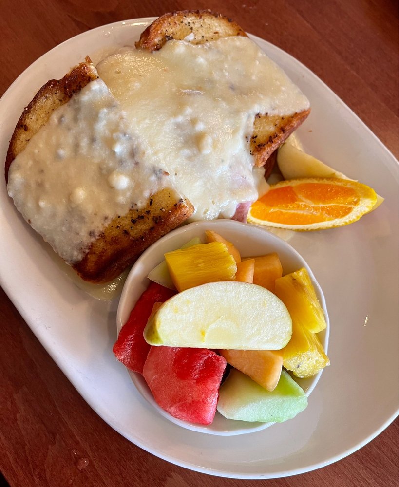 A chicken cordon bleu sandwich with a bowl of fresh fruit.