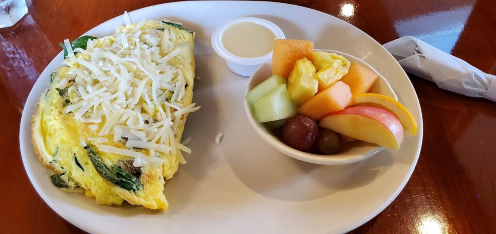 An omelet and a bowl of fruit on a white plate.