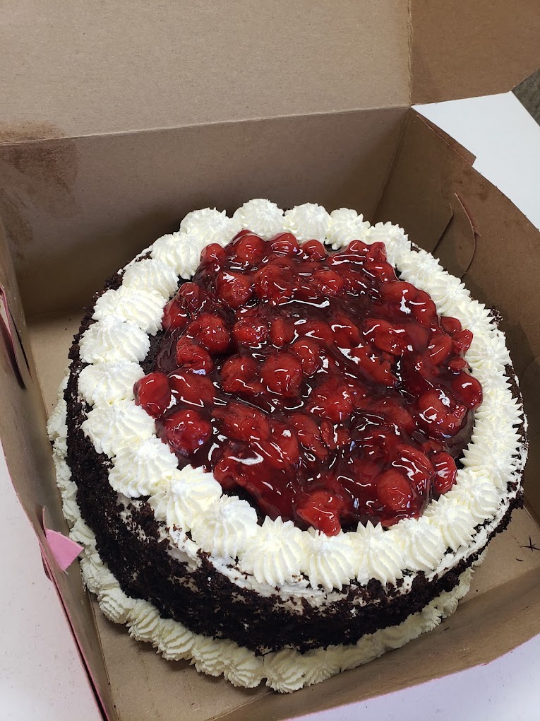 A massive cake with strawberries on top and chocolate crumb on the outside with piped white frosting.