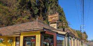 The outside of The Pancake Mill in North Bend, Oregon. The building is yellow, with brown trim and a brown roof. The sign is brown with yellow lettering.