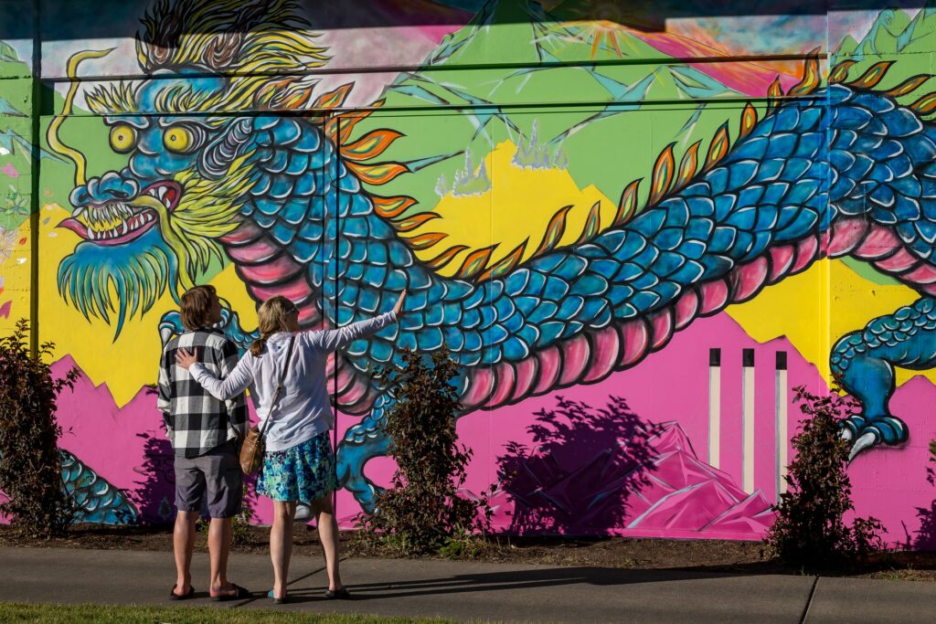 People look at a colorful pink, blue and green mural of a dragon.