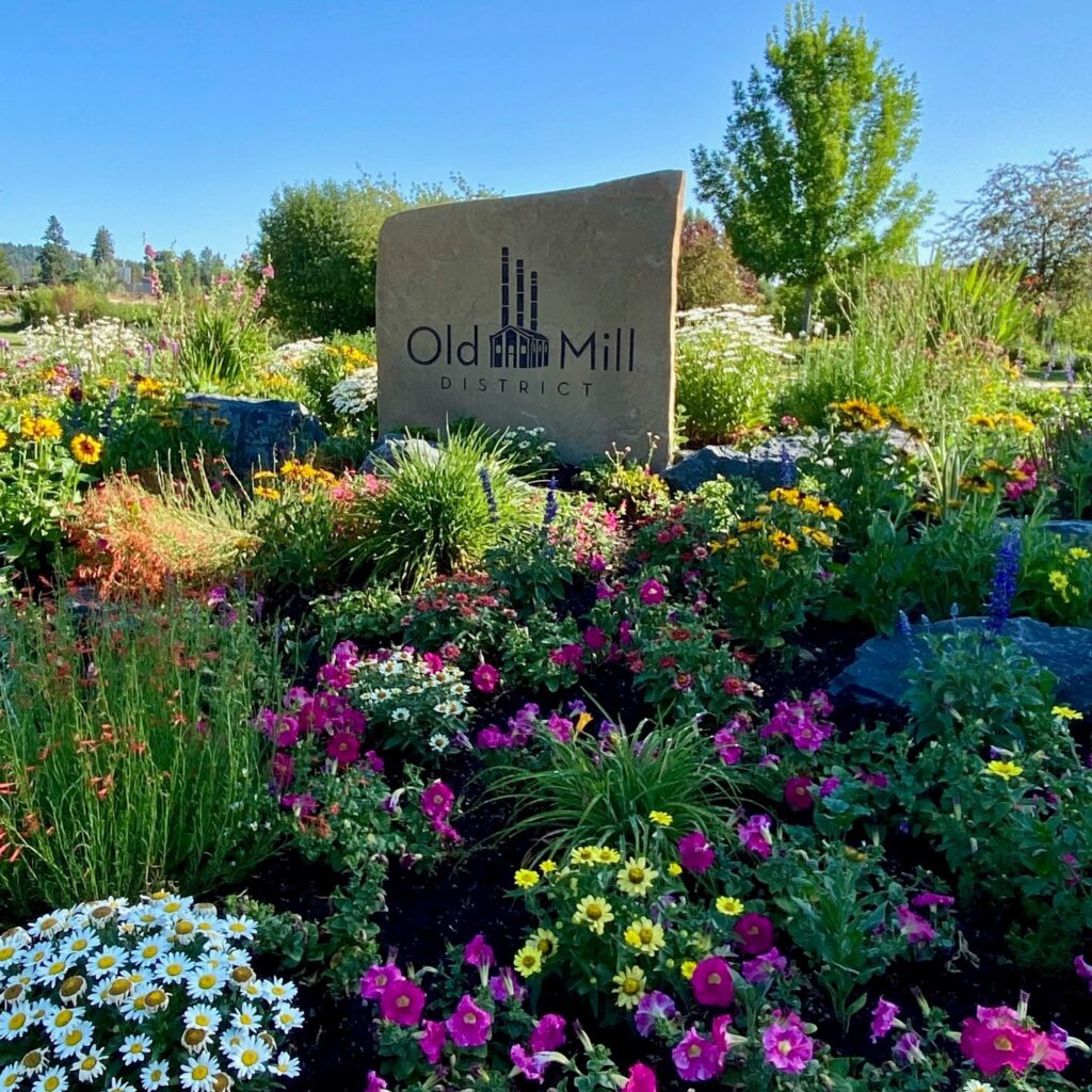 A variety of colorful flowers in front of a stone Old Mill District sign.