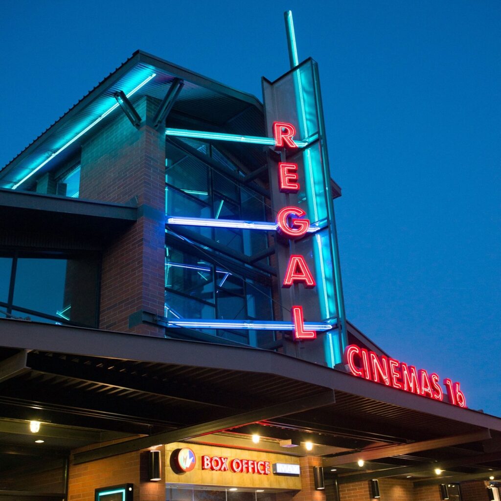 The outside of Regal Cinemas lit up at night with red and blue neon lights.