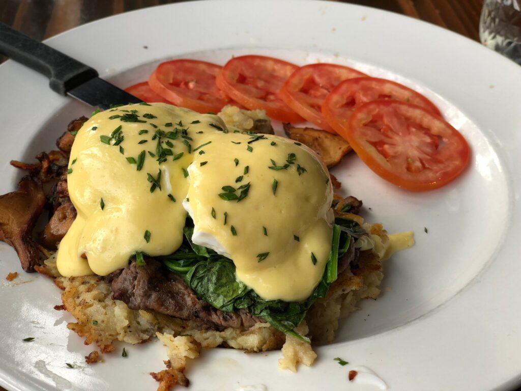 A tasty steak and eggs benedict with sliced tomatoes. Looks so good!