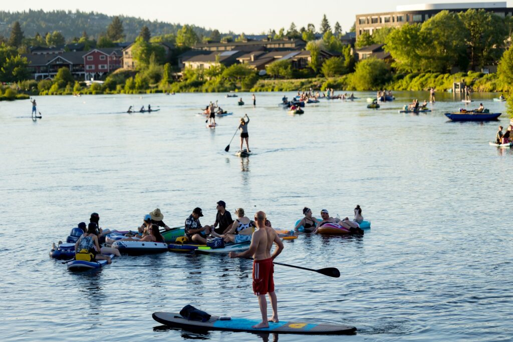 A round 50 people paddle and float in the Deschutes River at sunset.