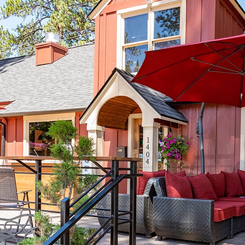 The outside of The Victorian Café in good weather. The building is red, and out front there's a red outdoor couch covered by a red umbrella. It looks cute.