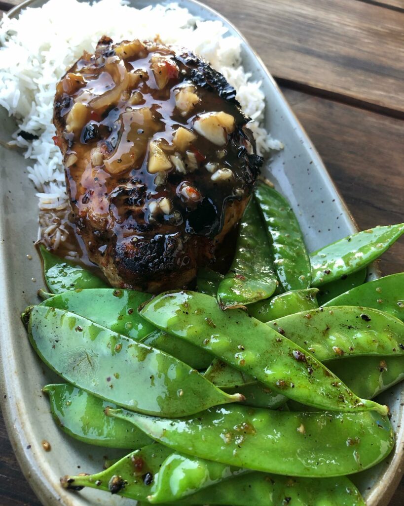 A delicious looking grilled meat on rice with snap peas.
