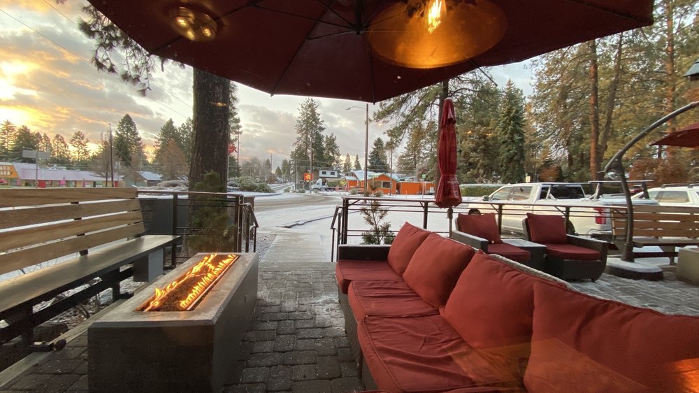 A red outdoor couch in front of a long rectangular fire pit and covered by a red umbrella. The ground outside is lightly dusted with snow.