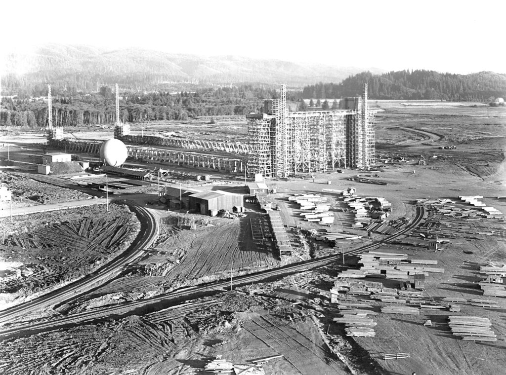 A black and white photo of massive Hangar B being constructed.  The air hangar was just started and there are piles of lumber everywhere ready to be used in construction. tillamook air museum, planes, WWII, history, family things to do, oregon coast