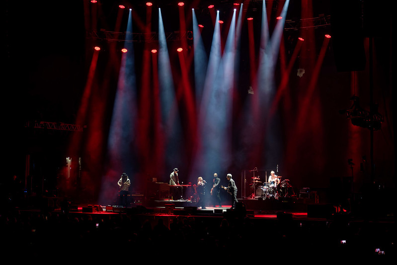 Alanis Morissette on stage. There are red and white spotlights from above illuminating Alanis Morissette and the band.