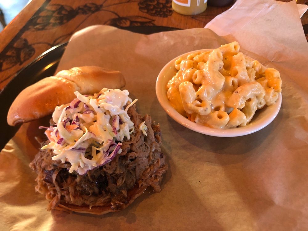 A meat sandwich with slaw on top and a bowl of mac and cheese.