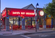 The exterior of Dave's Hot Chicken in Eugene, lit up at night. There is a red Neon Sign lit up that says Dave's Hot Chicken.