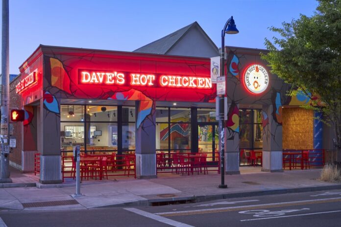 The exterior of Dave's Hot Chicken in Eugene, lit up at night. There is a red Neon Sign lit up that says Dave's Hot Chicken.