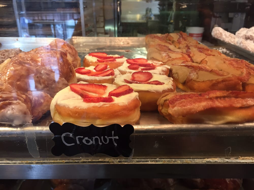 Several delicious looking varieties of donuts in a glass case, including donuts with sliced strawberries on top.