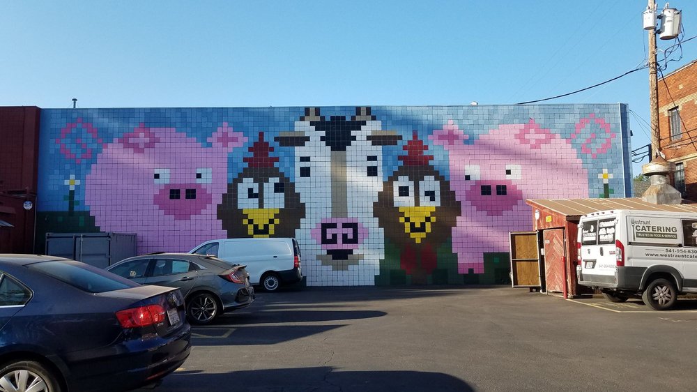 A painting of pixel art farm animals on the outside of the Bill and Tim's building. It's very colorful and playful.