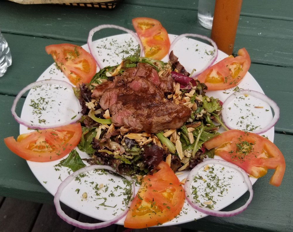 Steak salad. There are alternating onions and half cut tomato slices arranged in a circle around the salad. It looks really nice. The entire plate is dusted with a green herb.