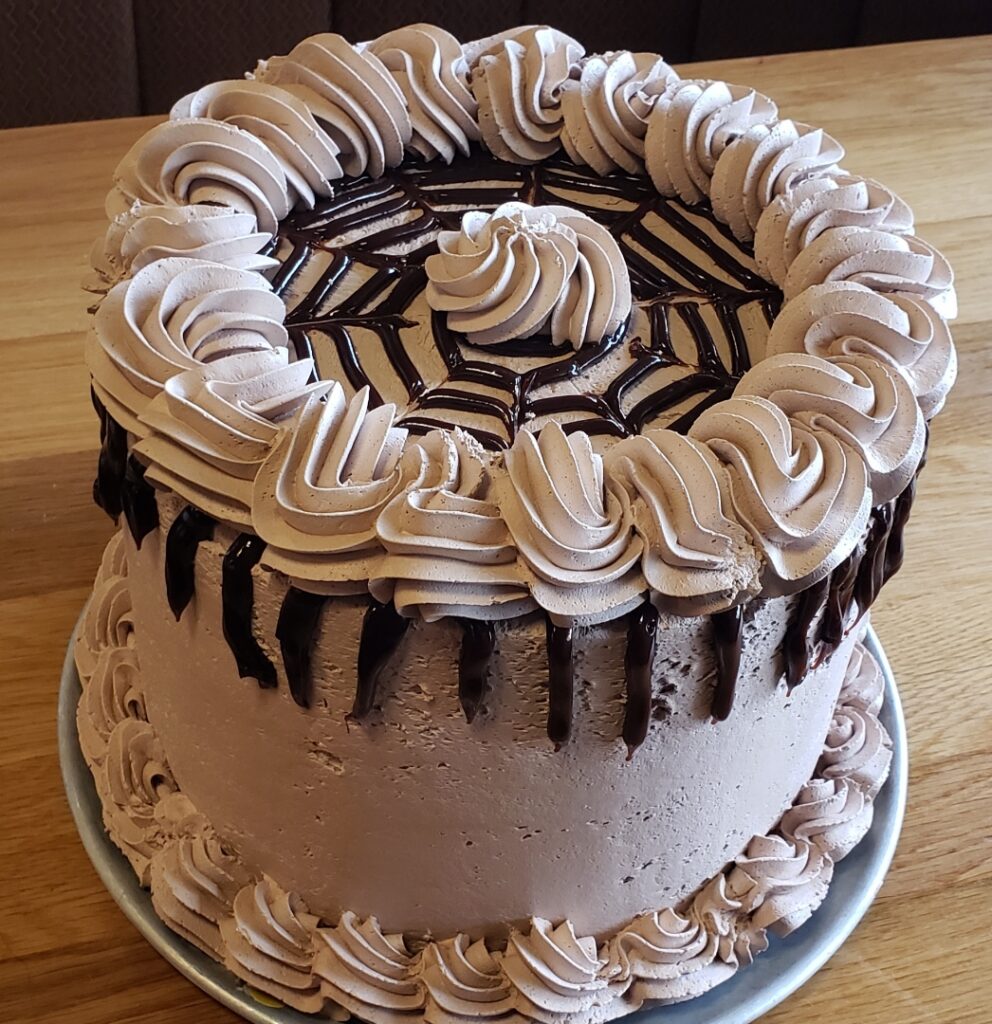 A whole five layer chocolate cake. It has brown frosting and drizzled chocolate in a web pattern over the top.