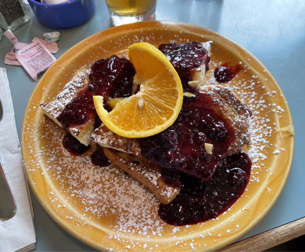 French toast. It has a slice of orange and a red marionberry sauce over top. The whole dish is sprinkled with powdered sugar. It looks absolutely delicious.