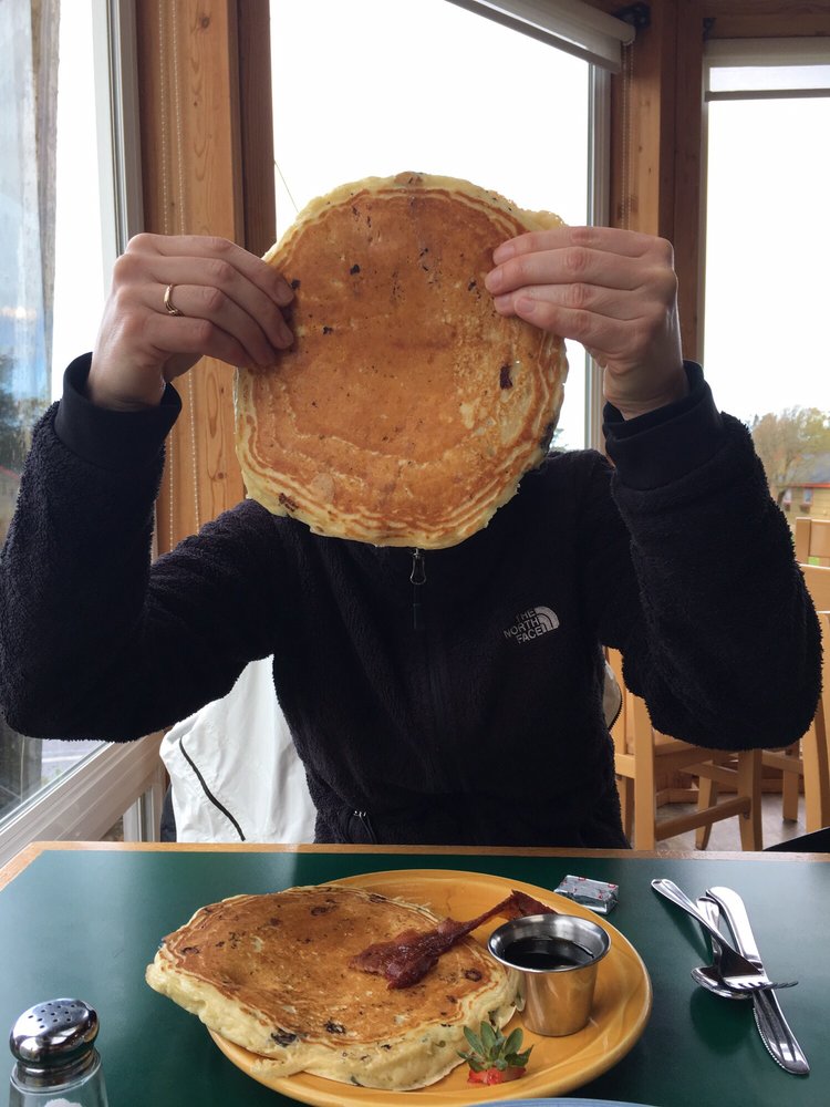 A person holds up a huge fluffy blueberry pancake in front of his face.