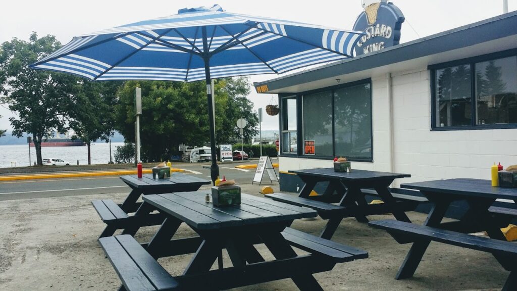 Outdoor seating at Custard King. It's wooden picnic benches under blue and white striped unbrellas.