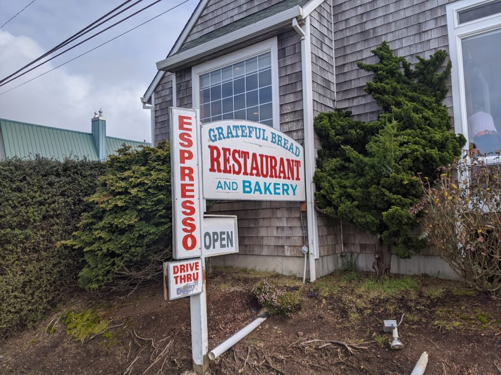 The outside of Grateful Bread Bakery. It looks like a gray beach cottage with wooden shingles as siding.